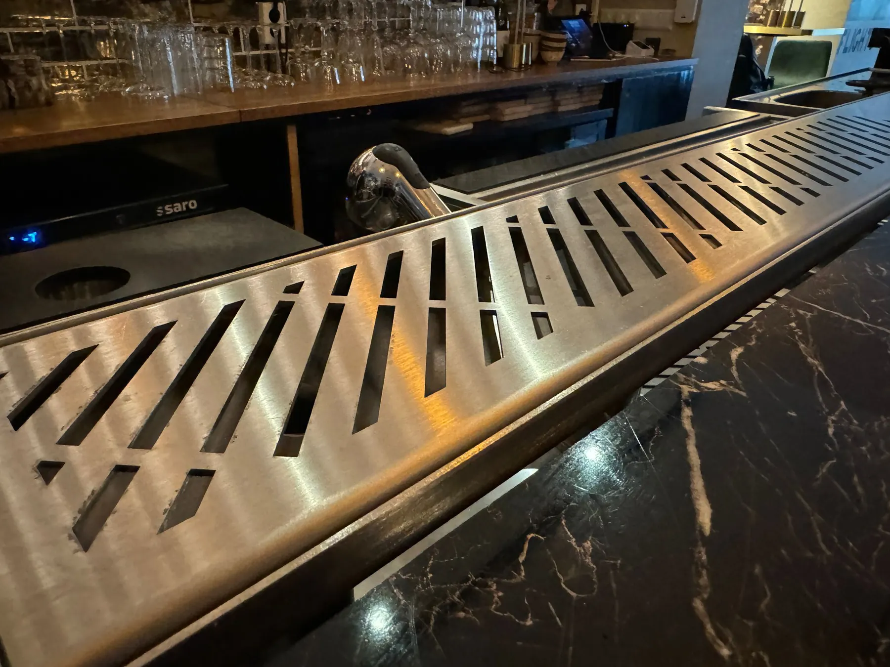 Stainless steel drink rail with integrated drain mounted along a bar